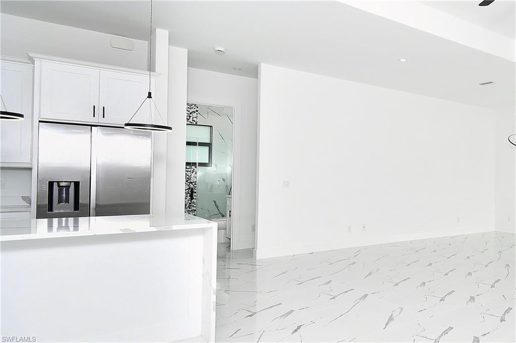 Bright kitchen area featuring white cabinetry, a stainless steel refrigerator, and a white countertop island