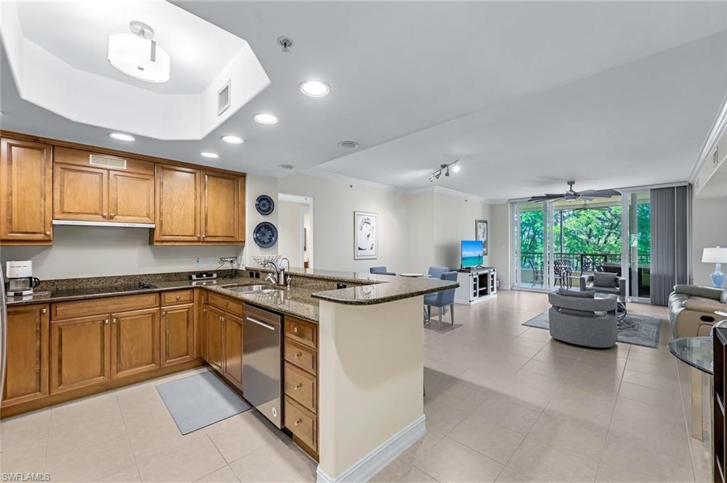 Kitchen with dark stone countertops, kitchen peninsula, dishwasher, sink, and ornamental molding