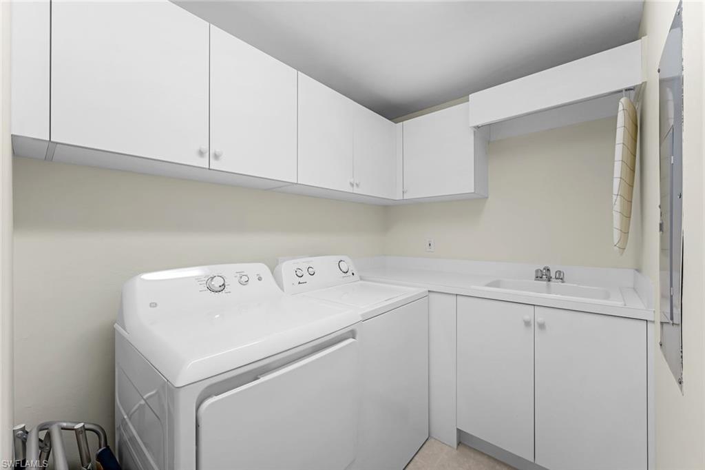 Laundry area with cabinets, light tile patterned floors, washer and clothes dryer, and sink