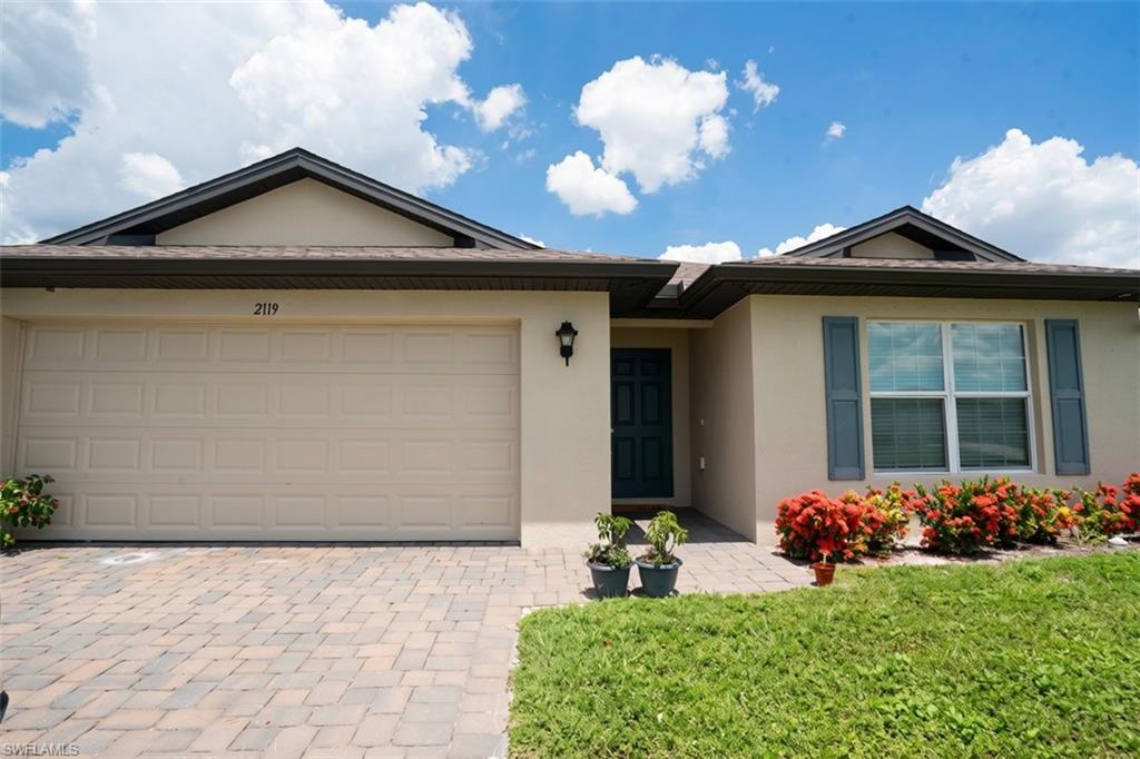 Cream stucco exterior with a dark front door, a two-car garage, and a paver driveway