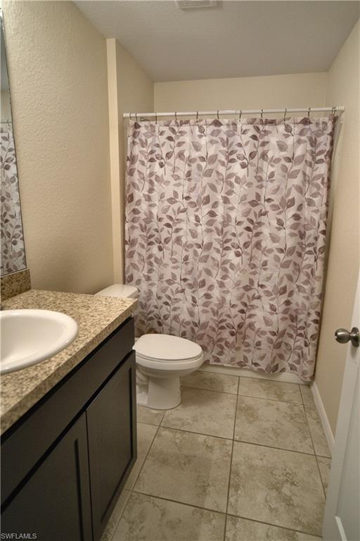 Bathroom featuring a dark wood-finish vanity with a built-in sink, a speckled countertop, tile flooring, and a white toilet