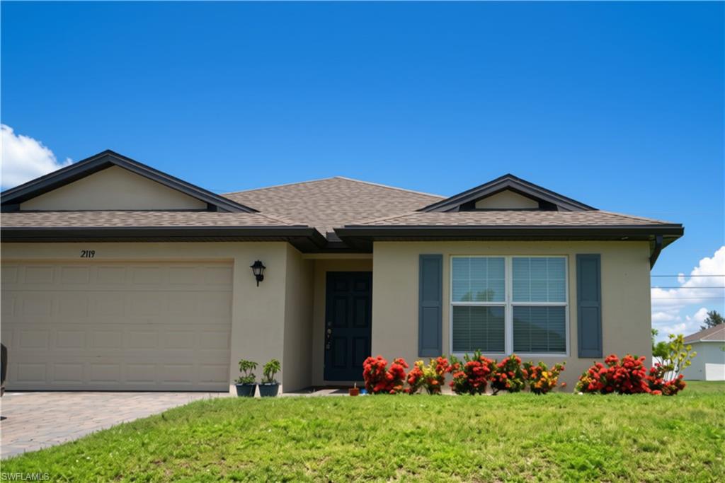 Stucco exterior with a shingle roof, featuring a two-car garage, front door with transom window, and a window with louvered shutters