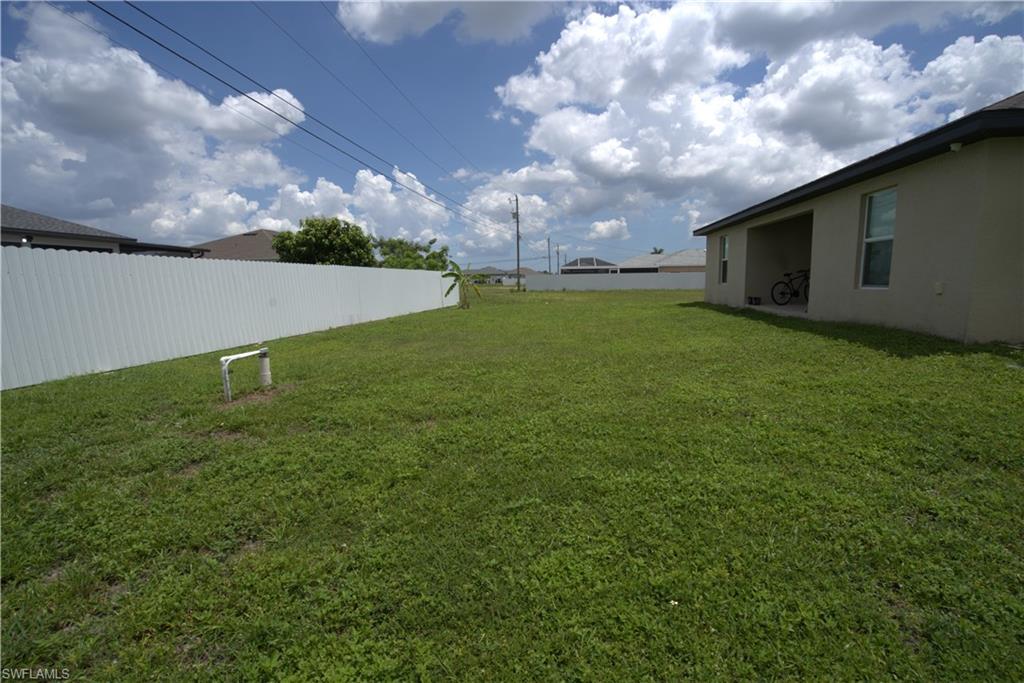 Expansive grassy yard area featuring a white privacy fence and a covered patio area