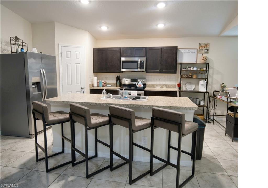 Kitchen featuring a breakfast bar with seating, recessed lighting, dark wood cabinetry, a stainless steel microwave, and tile flooring