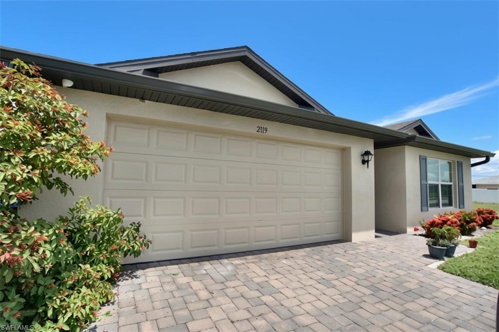 Exterior elevation featuring a two-car garage, paver driveway, and stucco finish