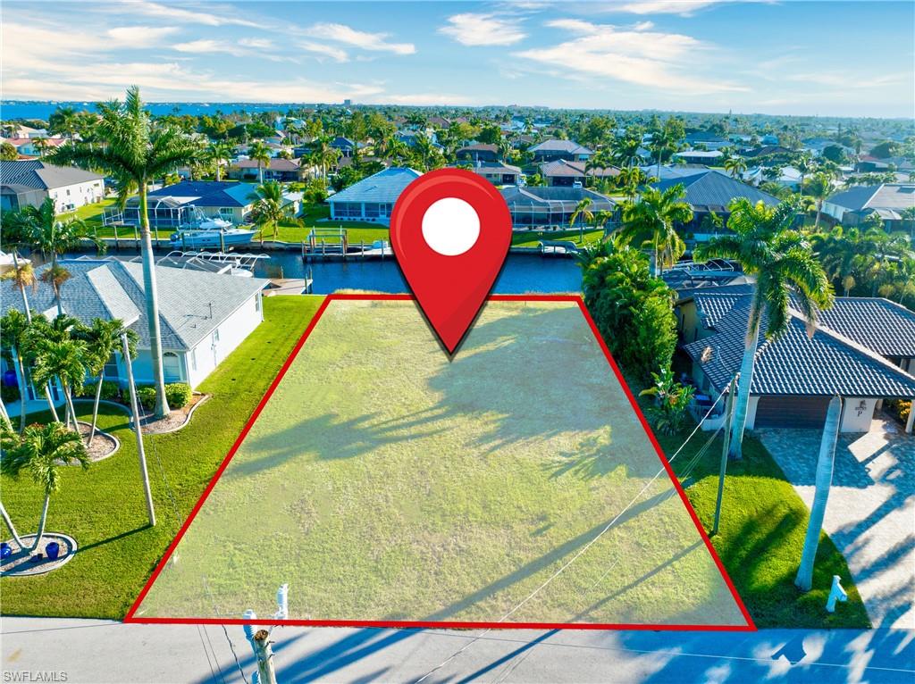 Cleared, level building lot featuring a waterfront canal, mature palm trees, and established surrounding properties