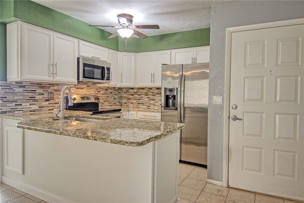 Kitchen featuring white cabinetry, a granite countertop island with an undermount sink, a mosaic tile backsplash, and stainless steel appliances including a refrigerator, microwave, and range