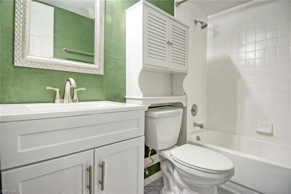 Full bathroom featuring a white vanity with integrated sink, brushed nickel faucet, decorative framed mirror, and a white tub with tiled shower surround