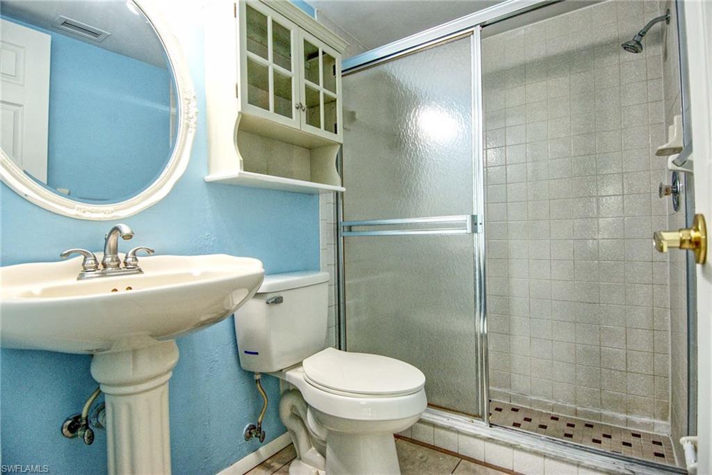Primary bathroom featuring a white pedestal sink, an ornate oval mirror, and an overhead storage cabinet with walk-in shower