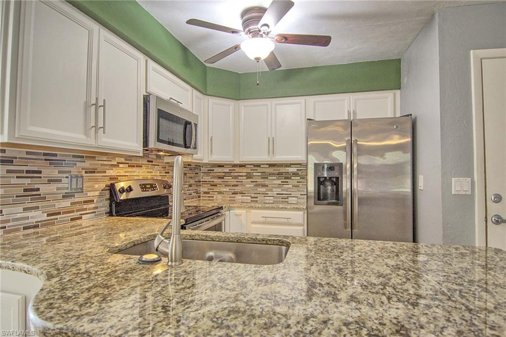 Kitchen featuring granite countertops, stainless steel appliances, white cabinetry, a mosaic tile backsplash, and a ceiling fan