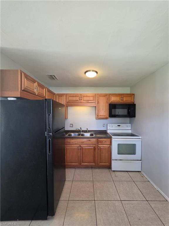 Kitchen featuring tile flooring, wood cabinetry, double basin sink, black refrigerator, and white electric range