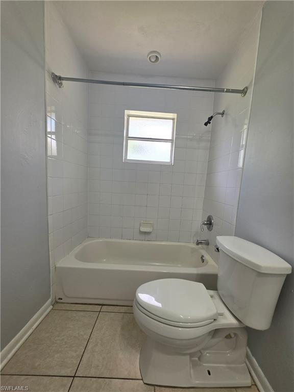 Bathroom featuring a white bathtub with tile surround, a white toilet, and a frosted window