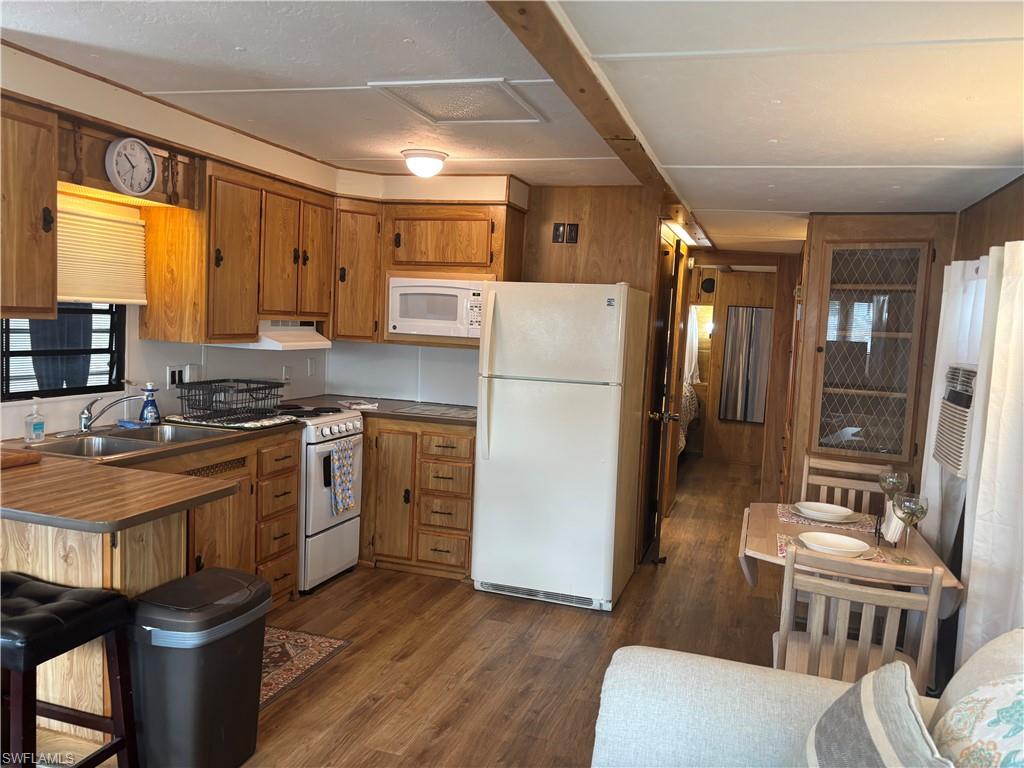 Kitchen featuring brown cabinetry, white appliances, dark wood-style floors, wood walls, and a breakfast bar area