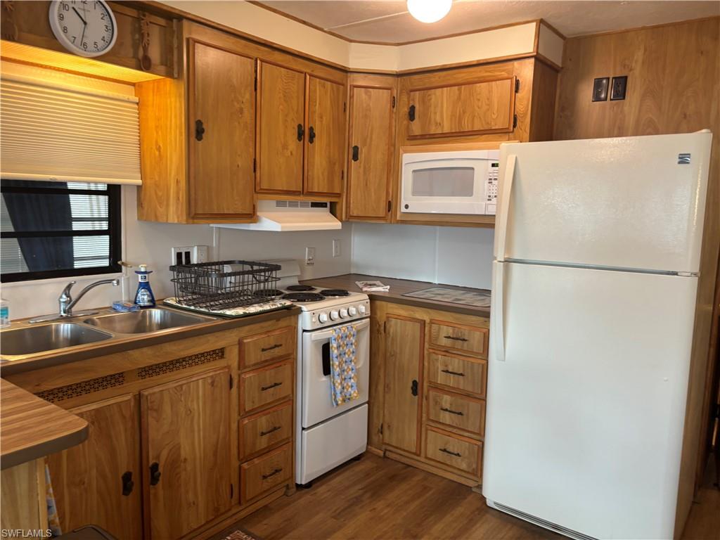 Kitchen with white appliances, dark wood-style floors, brown cabinetry, and under cabinet range hood