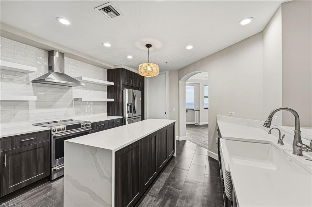 This kitchen has been thoughtfully reimagined, showcasing an oversized island with striking waterfall quartz countertops, a farmhouse sink, and stainless steel appliances. A spacious walk-in pantry and distinctive storage shelving provide exceptional functionality, while a classic subway tile backsplash, warm wood cabinetry, and custom lighting complete the space with refined style.