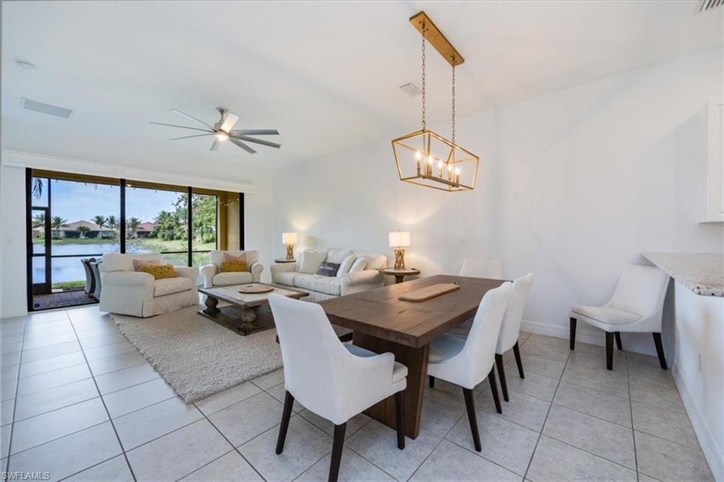 Tiled dining area featuring ceiling fan with notable chandelier and a water view