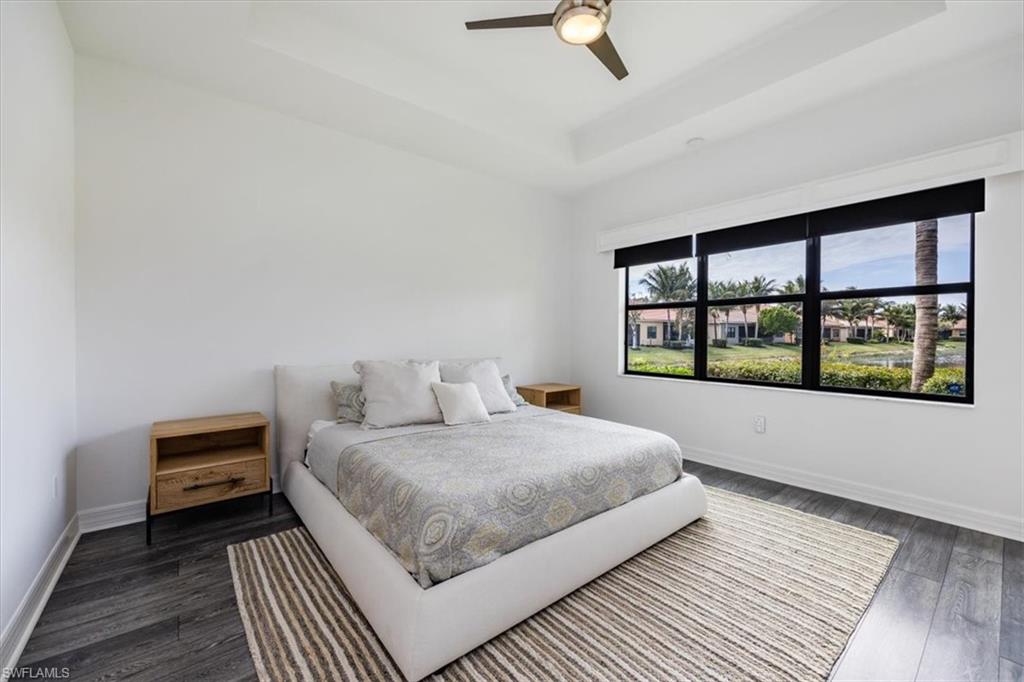 Bedroom with dark wood-type flooring, ceiling fan, and a tray ceiling