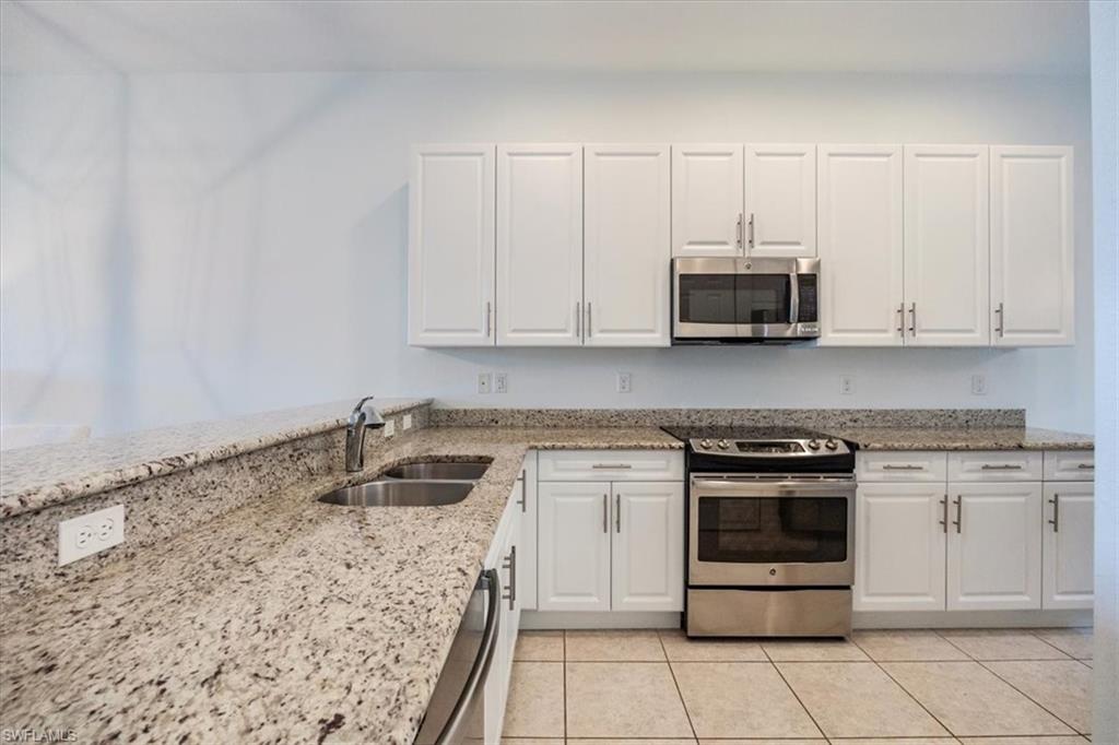 Kitchen with light stone counters, stainless steel appliances, light tile patterned floors, white cabinets, and sink