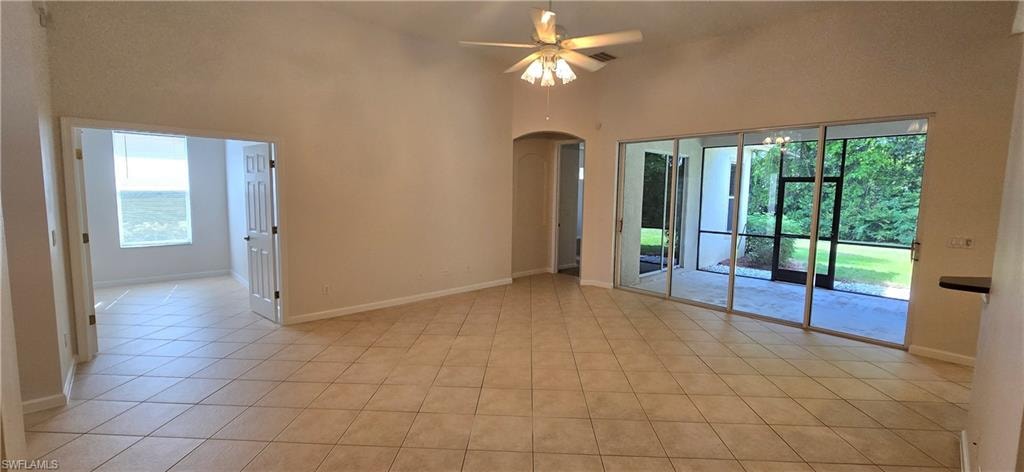 Large room, high ceiling, arched walkways, ceiling fan, and light tile patterned floors
