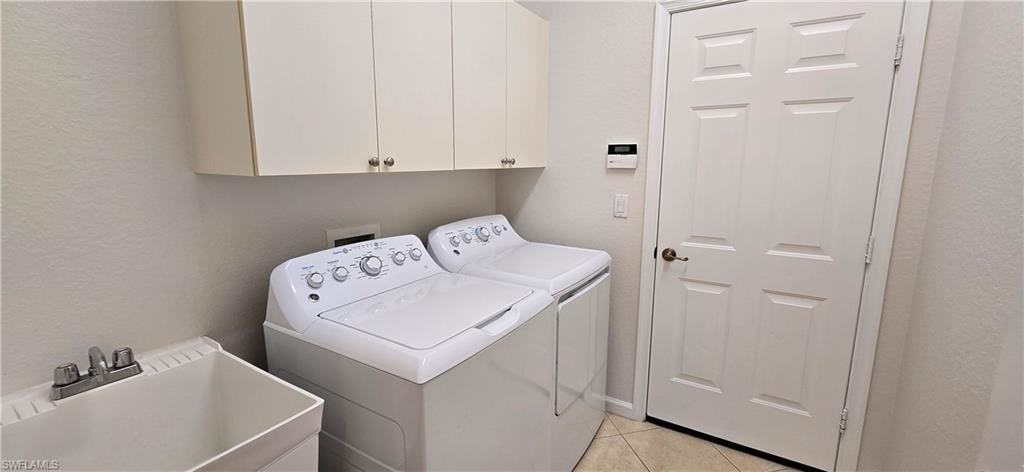 Laundry room featuring a textured wall, light tile patterned floors, separate washer and dryer, and cabinet space