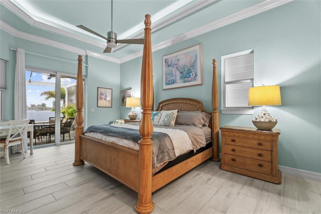 Recessed tray ceiling with crown molding, wood-finish flooring, and sliding glass doors opening to an outdoor patio with water frontage