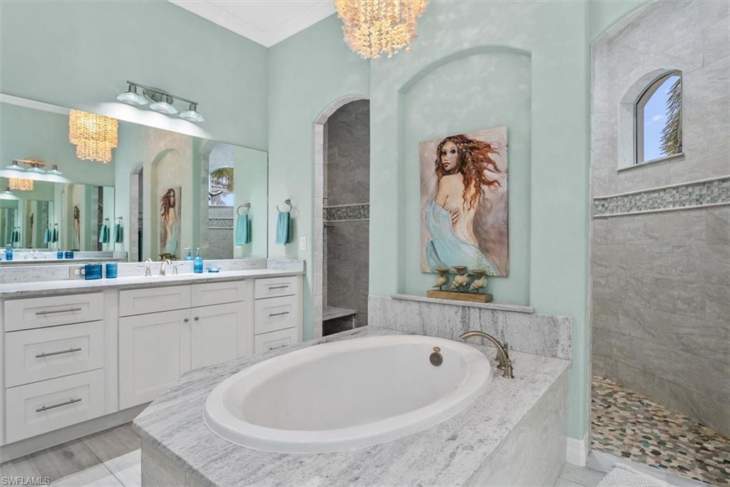 Soaking tub with a granite surround, dual vanity with white cabinetry, granite countertops, and a large mirror