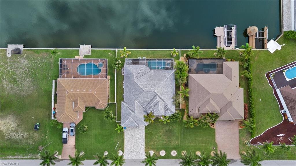 Waterfront property featuring a private boat dock, a screened-in swimming pool, a concrete tile roof, a paver driveway, and mature landscaping