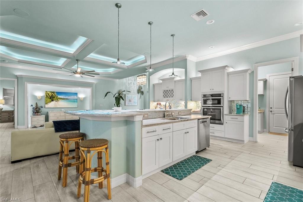 Open-concept kitchen featuring white cabinetry, stone countertops, stainless steel appliances, and wood-finish flooring