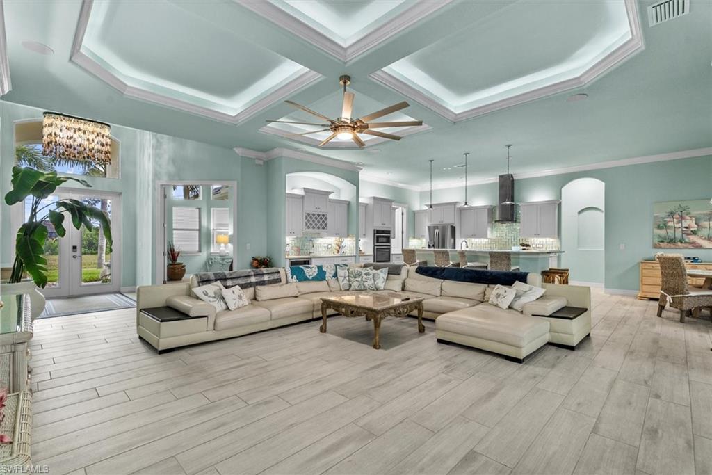 Spacious living area featuring wood-finish flooring, a tiered tray ceiling with recessed lighting and a ceiling fan, and an open-concept design to the kitchen