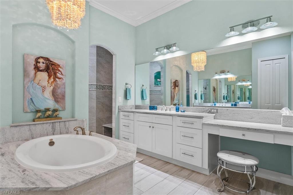 Spacious bathroom featuring a built-in tub, dual vanities with white cabinetry, extensive countertop space, and a large wall-mounted mirror
