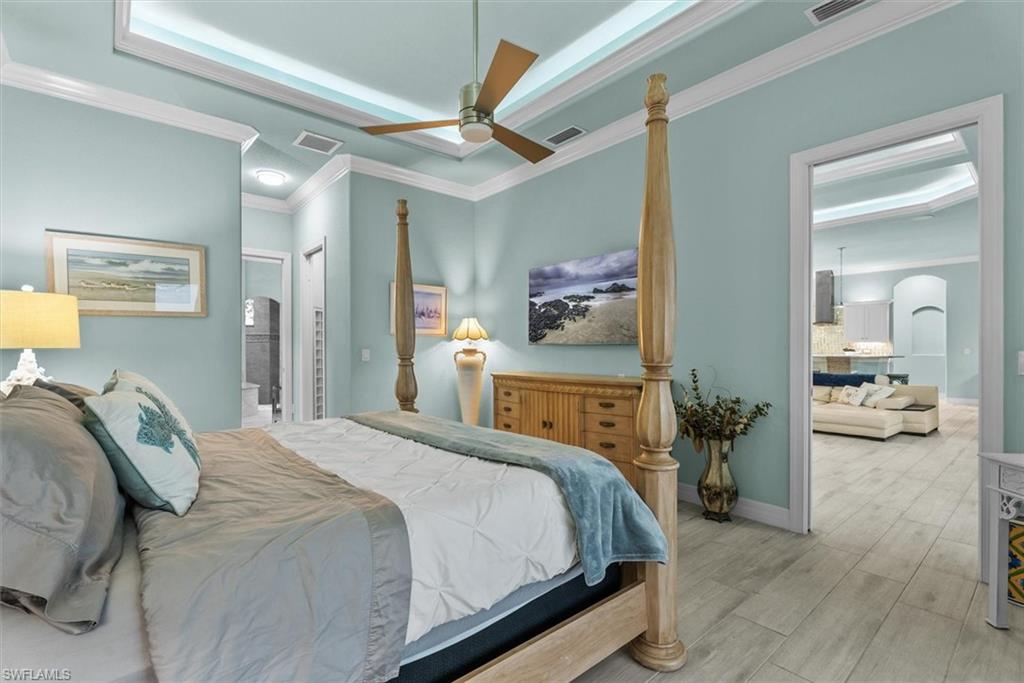 Bedroom with tray ceiling, crown molding, a ceiling fan, and light wood-finish flooring