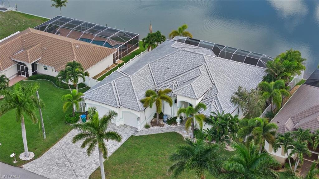 Waterfront residence featuring a paver driveway, lush tropical landscaping, and a screened-in pool enclosure
