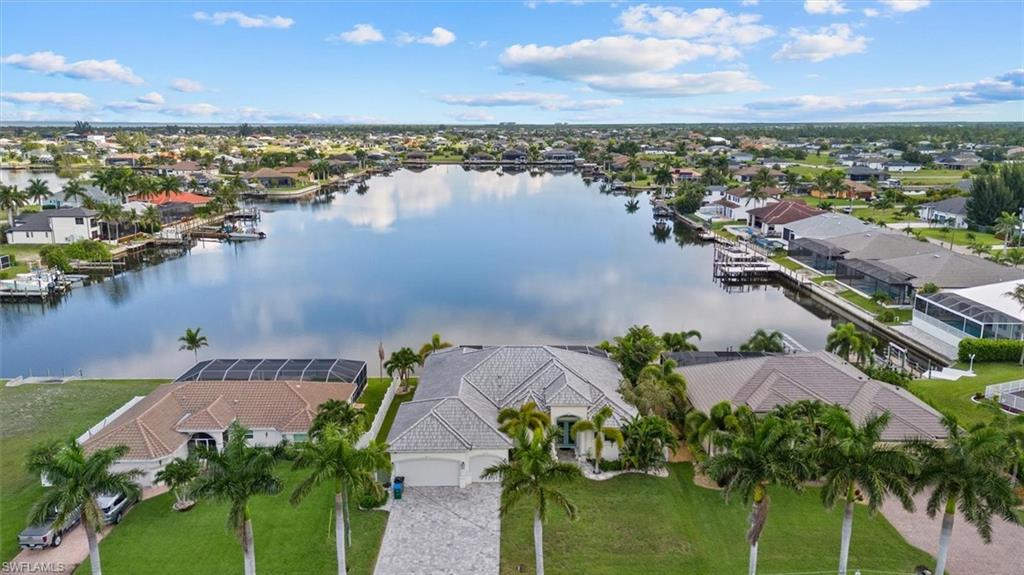 Waterfront property featuring a spacious lot with mature palm trees, a concrete paver driveway, and a screened lanai overlooking the canal