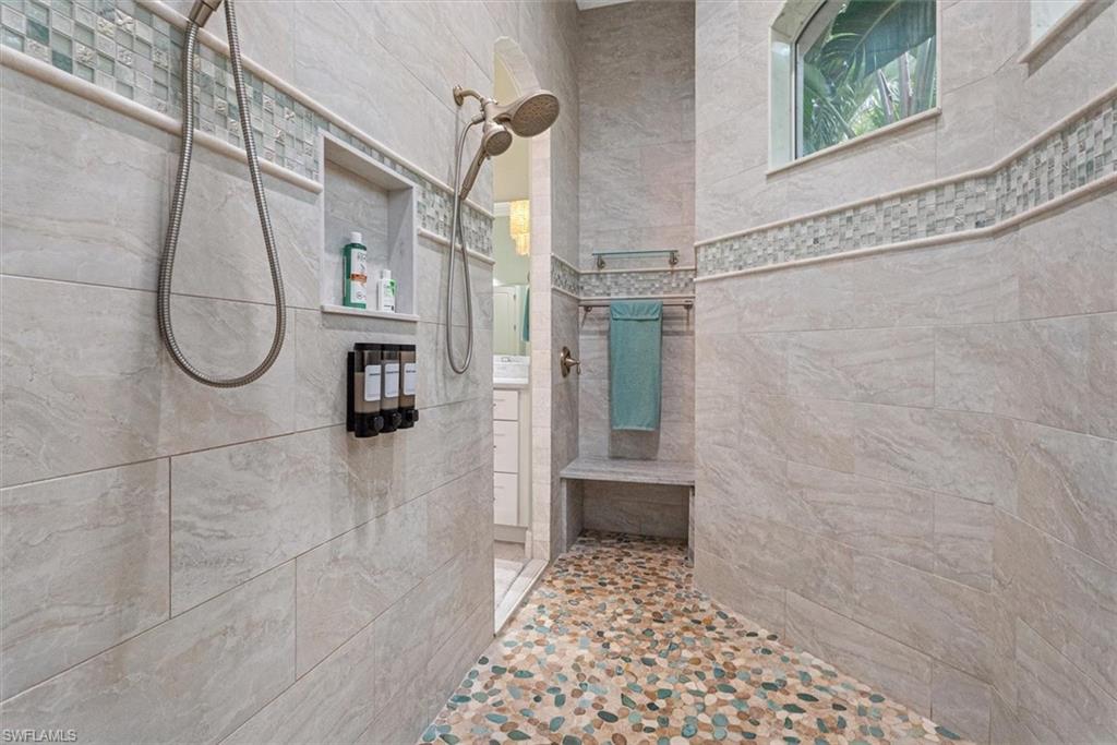 Spacious walk-in shower featuring a pebble-stone floor, light-toned tile walls with decorative mosaic accents, a built-in shower niche, and an integrated bench
