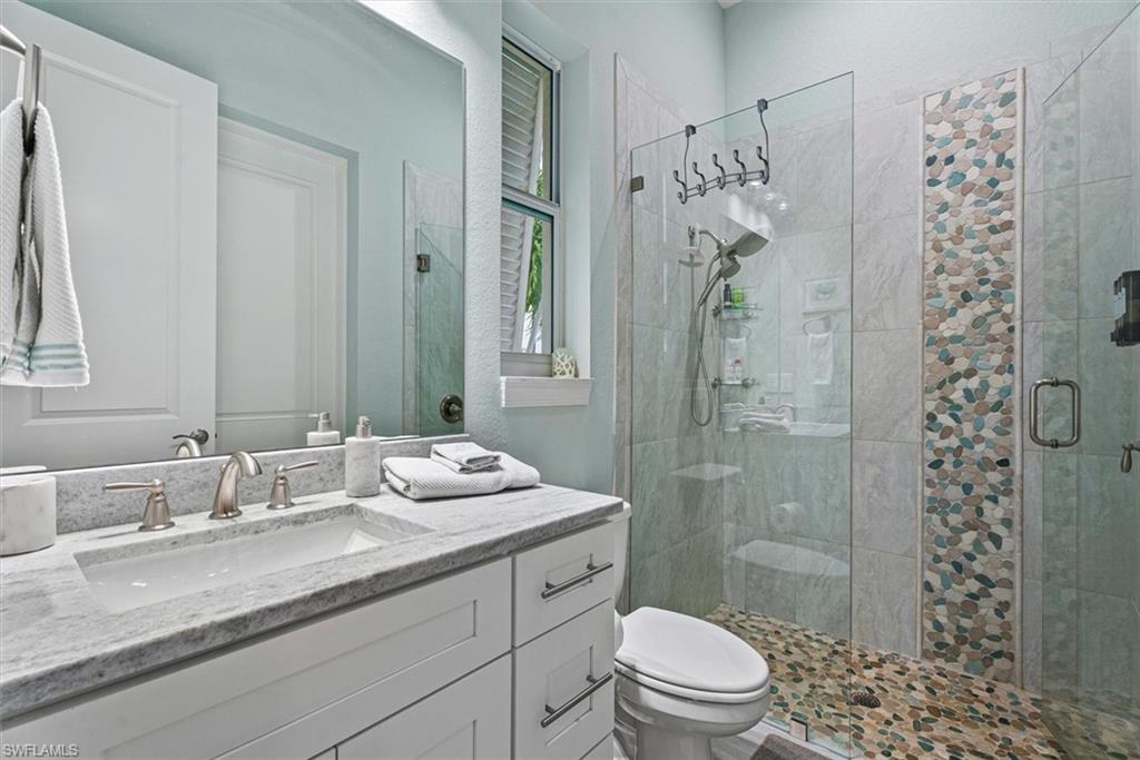 Bathroom featuring a walk-in shower with glass enclosure, pebble-tile flooring, and a decorative vertical accent tile