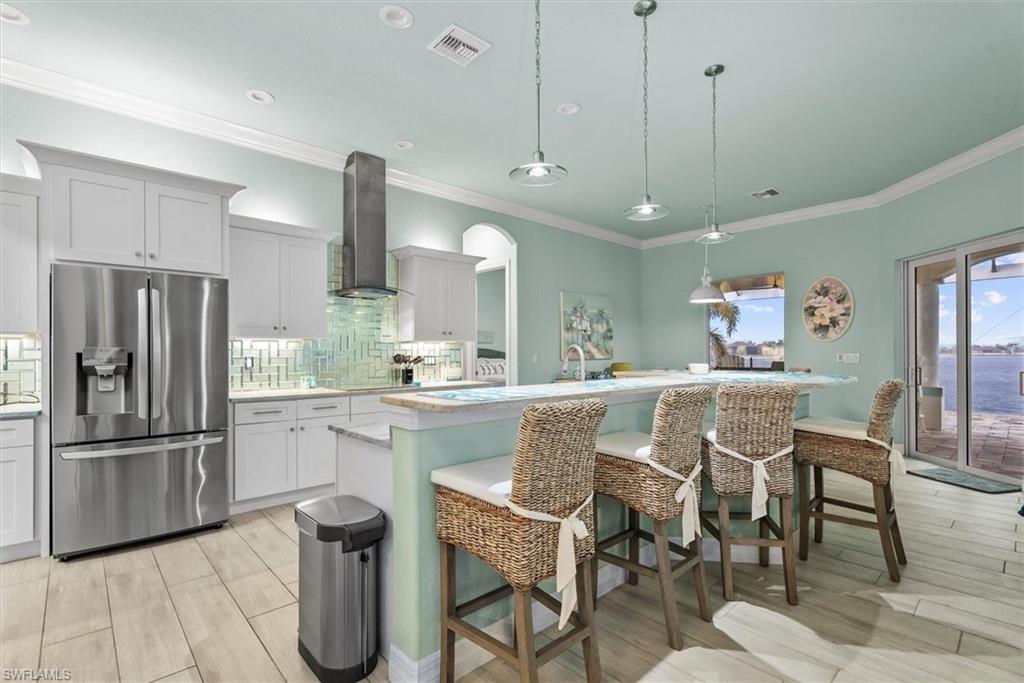 Gourmet kitchen featuring stainless steel appliances, custom white cabinetry, a glass tile backsplash, an eat-at island, and wood-finish flooring