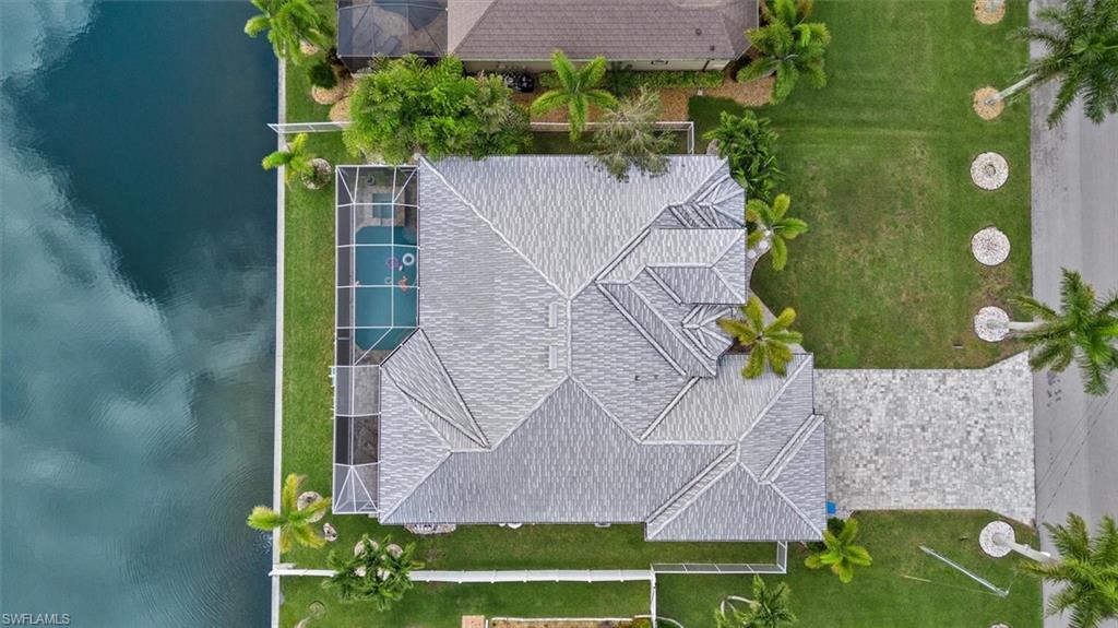 Property featuring a gabled roofline, screened-in swimming pool, paved driveway, canal frontage, and mature landscaping