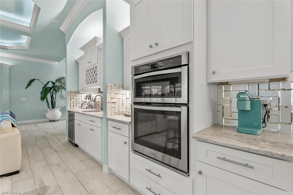 Integrated stainless steel double wall ovens, white shaker cabinetry, light-toned countertop, mirrored subway tile backsplash, and wood-finish flooring