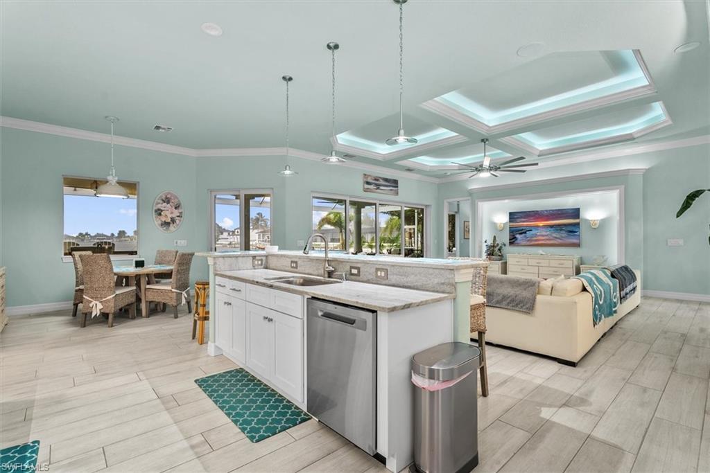 Open-concept living space featuring a kitchen island with stone countertops and an under-mount sink, integrated stainless steel dishwasher, and light wood-finish flooring