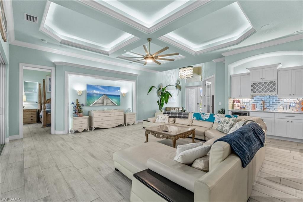 Living area with light wood-finish flooring, featuring a tray ceiling with integrated lighting and a ceiling fan