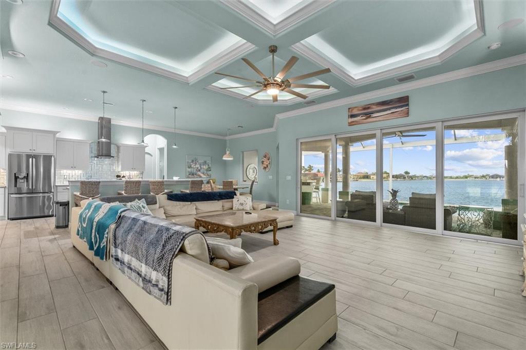 Expansive living area featuring light wood-finish flooring, a tray ceiling with recessed lighting and a ceiling fan, and sliding glass doors to the exterior