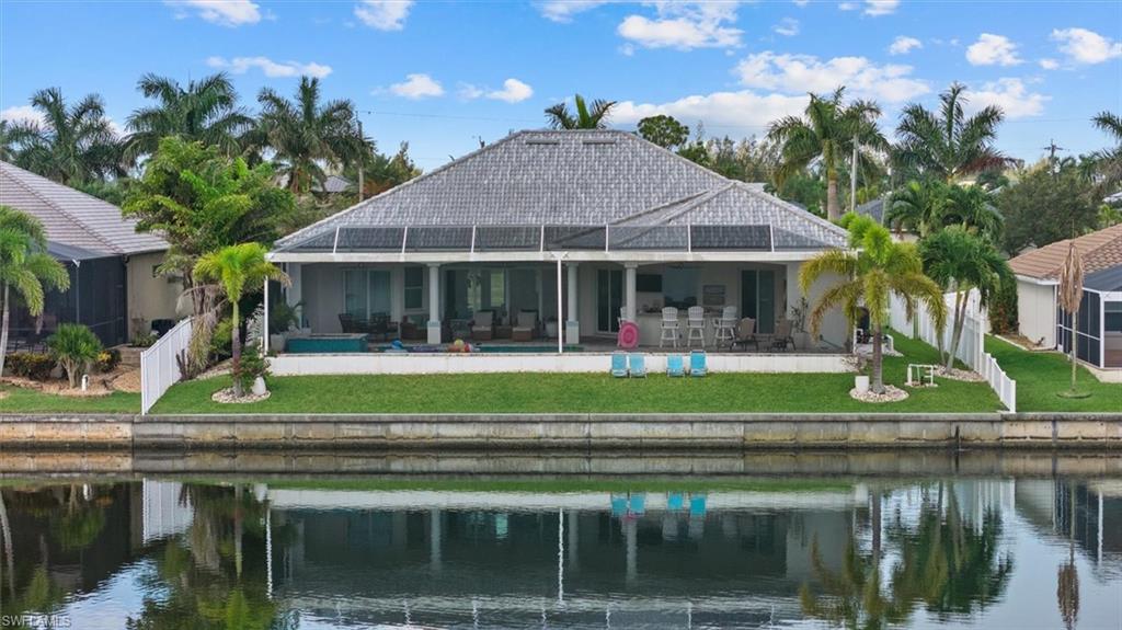 Waterfront property featuring a screened lanai, covered patio, outdoor kitchen, and tropical landscaping