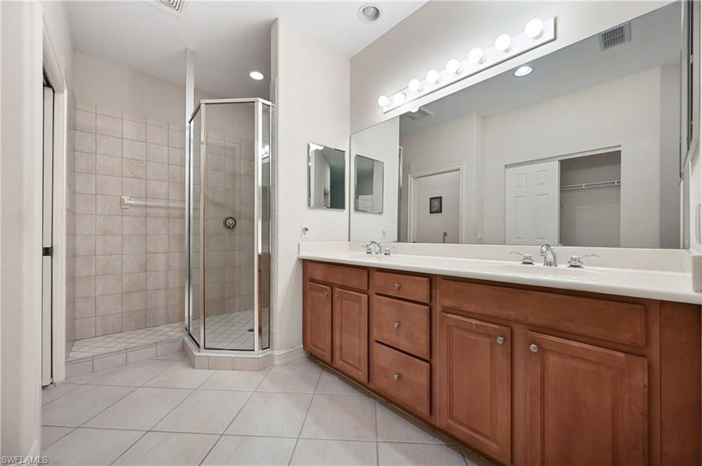 Dual sink vanity with wood-finish cabinetry, a large wall-mounted mirror, and a glass-enclosed shower