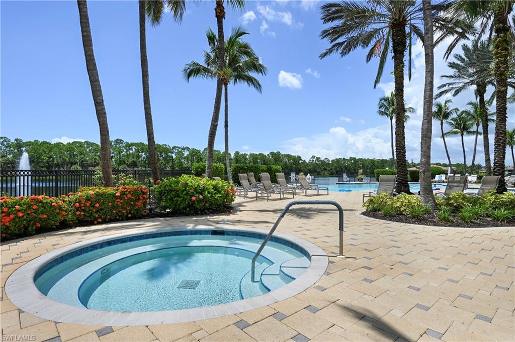 Resort-style pool area featuring a built-in spa, expansive paver decking, lush landscaping, and a water feature