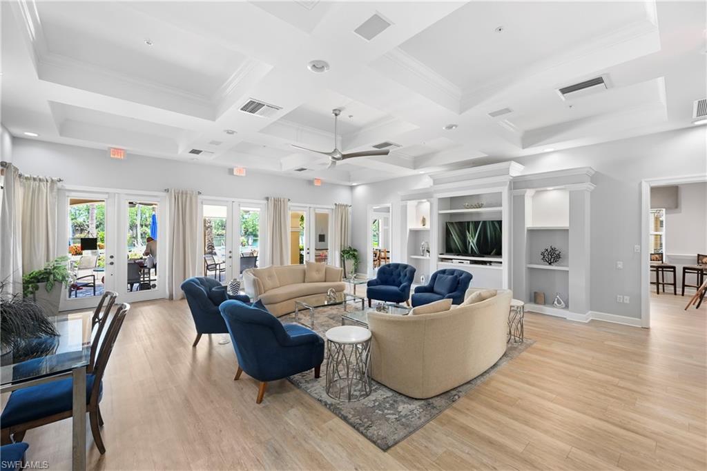 Spacious common area featuring light wood-finish flooring, multiple sets of French doors, built-in shelving, and tray ceilings with recessed lighting