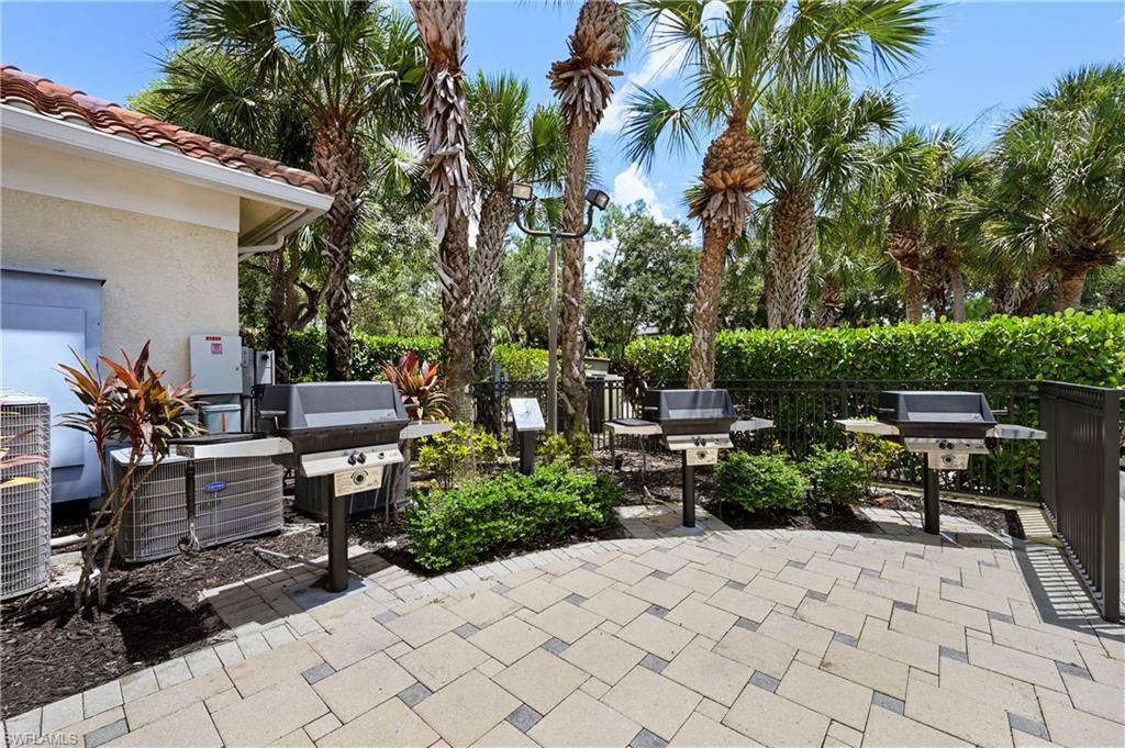 Paver patio with multiple grills, surrounded by mature palm trees and lush landscaping
