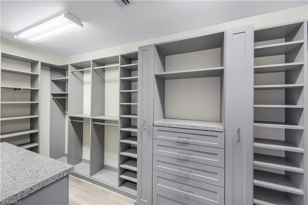 Custom-built primary suite walk-in closet #1 featuring extensive built-in shelving, multiple hanging rods, closed cabinetry, a central island, and drawer storage