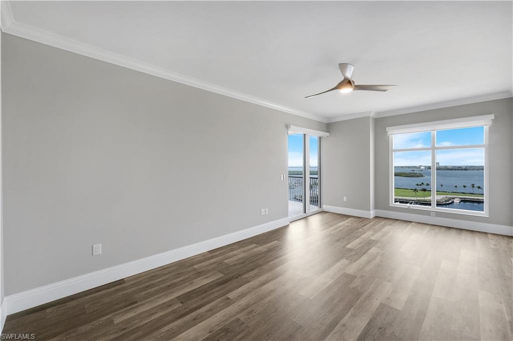 Spacious primary suite with waterfront views featuring wood-finish flooring, a contemporary ceiling fan, and crown molding