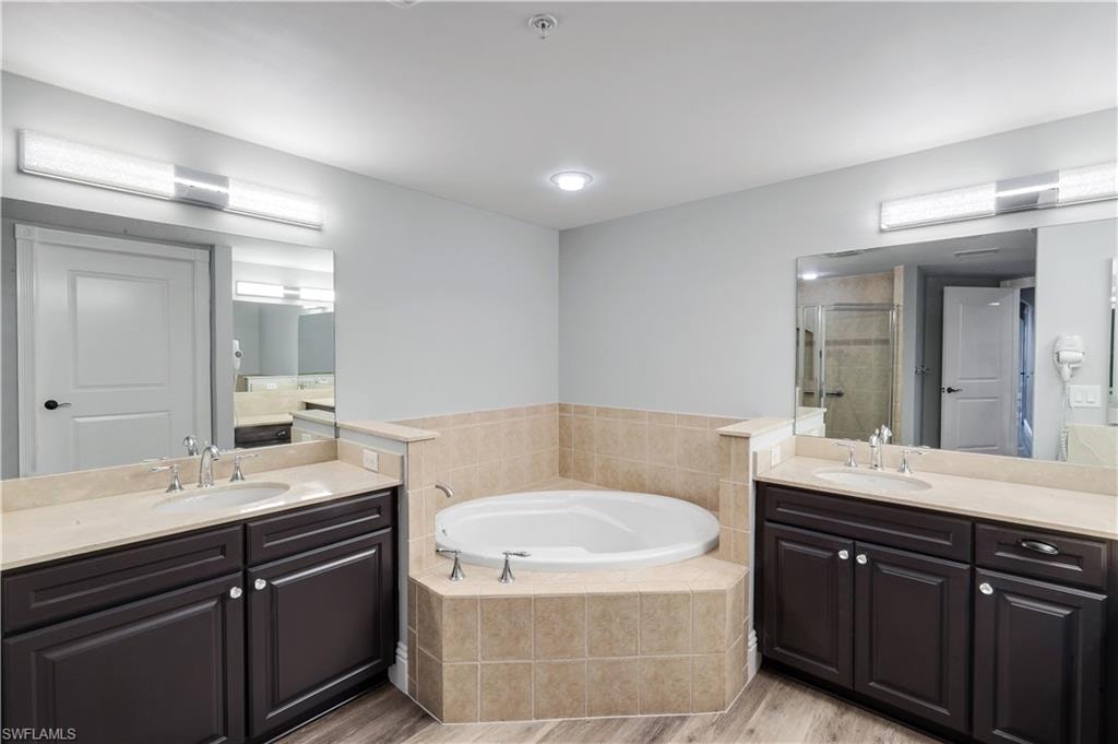 Primary bathroom featuring a built-in jetted tub surrounded by neutral-toned tile, flanked by dual vanities with dark wood cabinetry and light-toned countertops