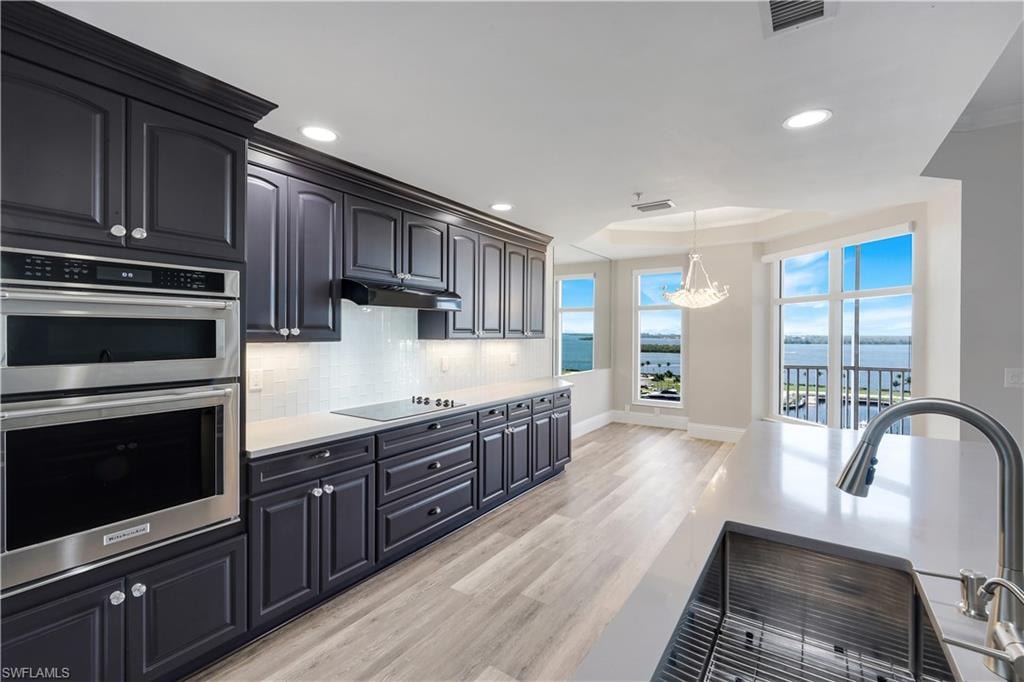 Kitchen featuring dark wood cabinetry, light countertops, built-in stainless steel double ovens, and a tile backsplash